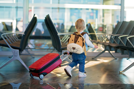 child walking in an airport with rolling suitcase and backpack