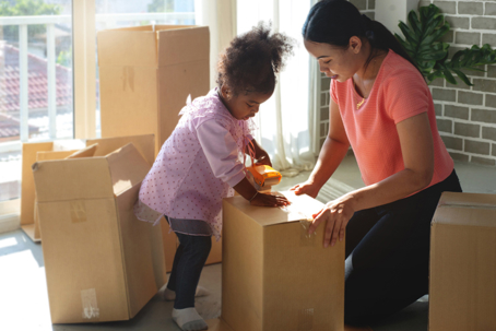 Mother and daughter stick tape on cardboard boxes at home