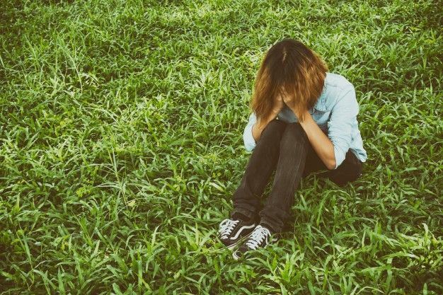 young woman sitting on the grass crying